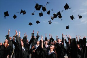 newly graduated people wearing black academy gowns throwing hats up in the air